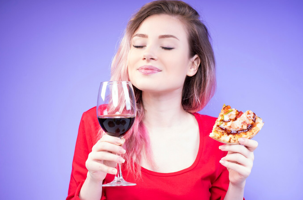 A young woman enjoying a wine with a slice of pizza