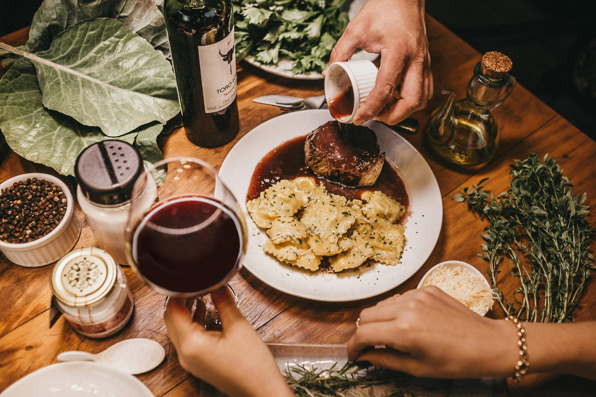 Pouring sauce on a steak with a glass of wine on the table